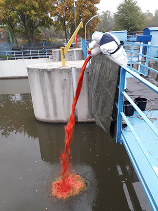 Mitarbeiter steht auf einer Brücke und schüttet Farbstoff aus einem Kanister ins Gewässer